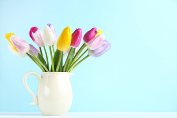 Bouquet of tulip flowers in jug on blue background