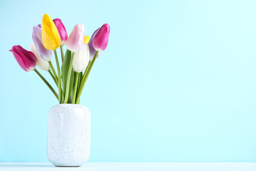 Fototapeta na wymiar Bouquet of tulip flowers in vase on blue background