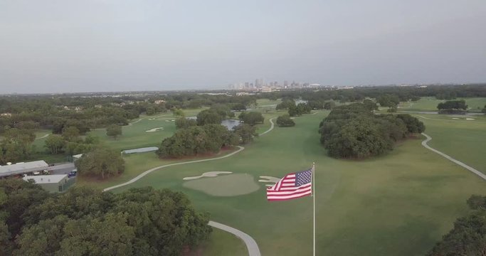 Aerial of an american flag flying in the wind over a golf course with New Orleans skyline in the distance