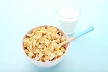 Corn flakes in bowl with glass of milk on blue background