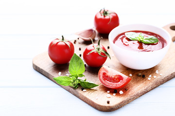 Ketchup in bowl with basil leafs and spices on wooden table