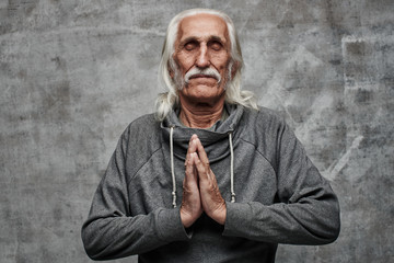 The pacified gray-haired grandfather folded his palms in prayer position, meditation, relaxation, forgiveness, keep calm. Gray studio background
