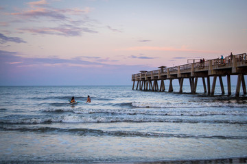 People surfing by pier in the sunset