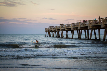 People surfing by pier in the sunset