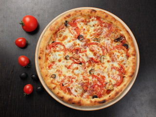 Pizza with sausage, olives, tomatoes and pickled cucumbers on a plate