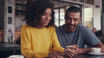 Young couple sitting together in cafe looking at mobile phone - Powered by Adobe