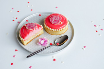 Mousse mini tarts covered with pink glaze and decorated with chocolate elements on white plate on white background