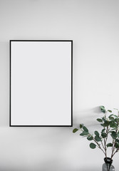 Composition of empty black wooden frame install on white painted wall with artificial plant on the corner / interior design / isolated object with composition