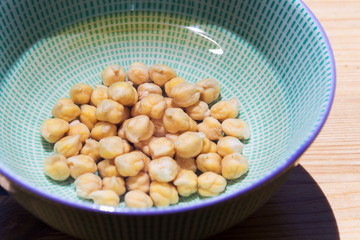 Chickpeas soaked in bowl with water before cooking to shorten cooking time, wooden table background