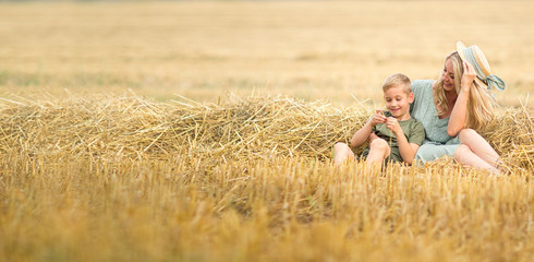 Family photo: mom blonde with long hair in a straw hat and son playing in the field. The family in the village. Family value. panorama