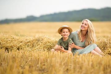Naklejka na ściany i meble Family photo: mom blonde with long hair in a straw hat and son playing in the field. The family in the village. Family value.