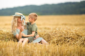 Family photo: mom blonde with long hair in a straw hat and son playing in the field. The family in the village. Family value.