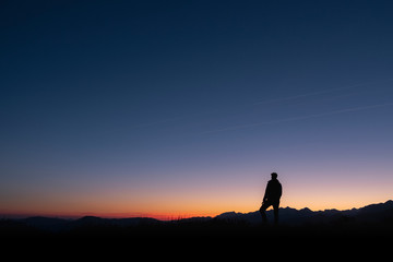 A man looks at the sun rising from the top of a mountain