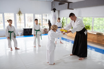 Cute blonde-haired boy taking yellow belt from his aikido teacher