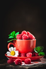 Raspberry in a red cup with chamomile and leaves on a dark background. Summer and healthy food concept. Selective focus. Background with copy space.