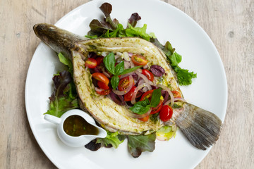 close up of baked sea bass fish mediterranean style with cherry tomatoes, olives, capers and basil