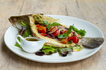 close up of baked sea bass fish mediterranean style with cherry tomatoes, olives, capers and basil
