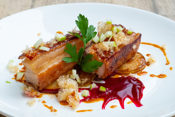 close up of crispy slow cooked pork belly in beetroot sauce and apple