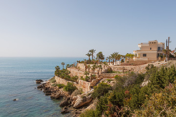 Fototapeta na wymiar Luxurious house with palms on the steep coast of Mediterranean sea. Cyprus, sunny summer day