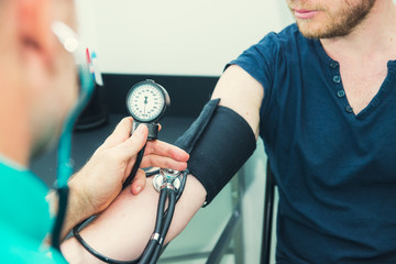Close up Male Doctor using sphygmomanometer with stethoscope checking blood pressure to a young...