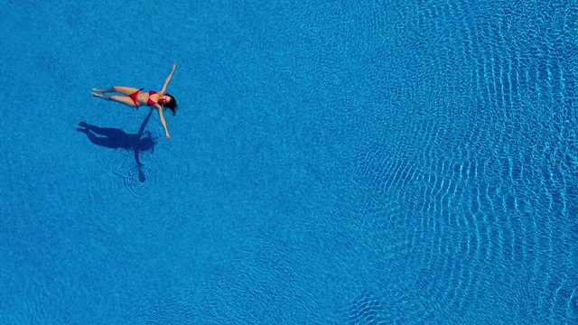 View from the top as a woman in a red swimsuit swims backstroke in the pool