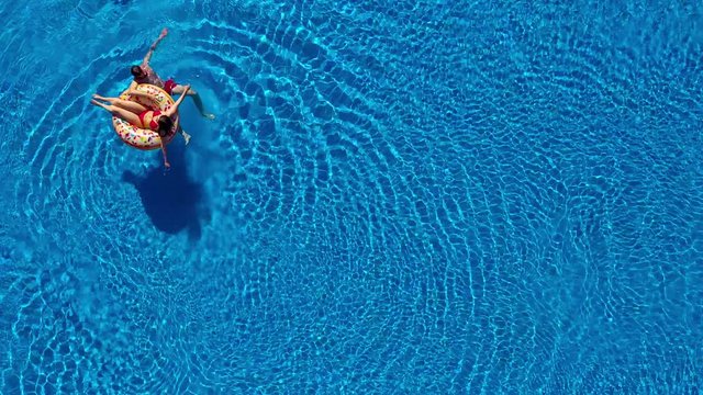 Aerial view of couple having fun in the pool, man is swimming and a woman is lying on an inflatable donut