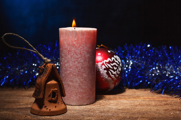 A burning candle and Christmas toys with tinsel stand on a wooden surface. Preparation and meeting...