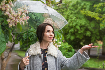 Woman in a coat on the background of green trees under an umbrella during the rain.