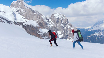 Two young women walking upwards on the snow in Dolomites with big backpacks
