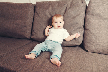 Little contented happy baby boy with pacifier sitting on a bed or a sofa. The first year of life in the family.