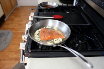 Steelhead frying in a stainless steel pan with the skin side down.