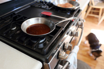 Demi glace or brown glaze cooking in a stainless steel skillet on the stove top.