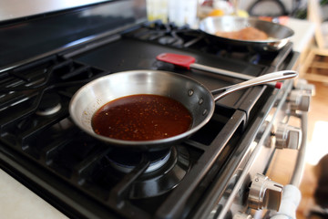 Demi glace or brown glaze cooking in a stainless steel skillet on the stove top.