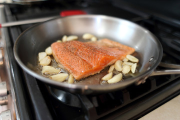 Steelhead frying in a stainless steel pan with the skin side down.