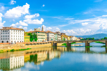 Ponte alle Grazie bridge over Arno River blue reflecting water and old buildings on embankment promenade in historical centre of Florence city, blue sky white clouds, Tuscany, Italy