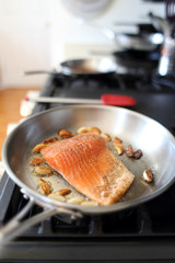 Steelhead frying in a stainless steel pan with the skin side down.