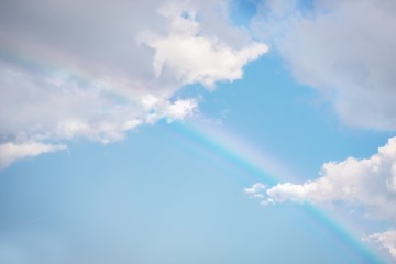 Naklejka na ściany i meble A bright rainbow in the blue sky. White fluffy clouds. Copy space