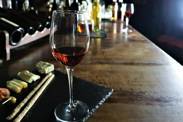 Glass of red wine,  olives, prosciutto, salami, aged cheese on a table at a cozy  bar.