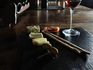 Glass of red wine,  olives, prosciutto, salami, aged cheese on a table at a cozy restaurant