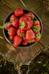 top view of red fresh strawberries in bowl on stump