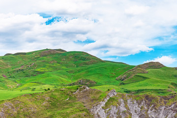High hills with green grass blue sky with clouds.