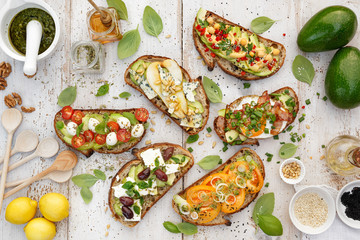Assorted  open faced sandwiches, Open avocado sandwiches made of  slices of sourdough bread with  various toppings on a white wooden table, top view