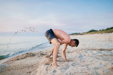 Man on the beach digging hole in sand beyond the sea in summer.