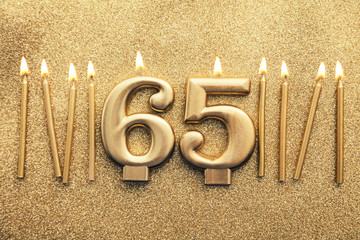 Number 65 gold celebration candle on a glitter background