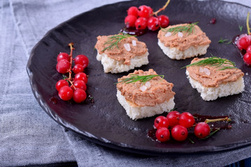 Canape with foie gras on the black plate. Red currant berries around