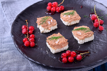 Canape with foie gras on the black plate. Red currant berries around