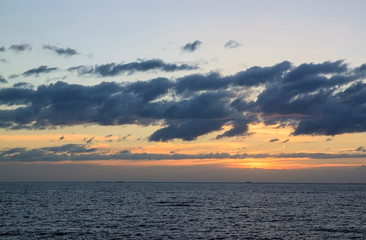 Scenic sunset over the sea. The sun sets on the water. Clouded sky is painted with bright colors. Sunset beach in a summer evening. Gulf of Finland,  Baltic sea,  Saint-Petersburg, Russia.