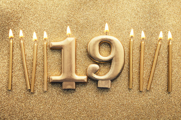 Number 19 gold celebration candle on a glitter background