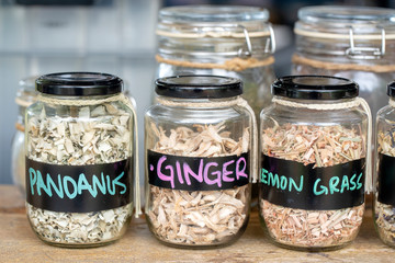 Assortment of dried spices in glass bottles on wooden background. Dry ginger, pandanus, lemon grass in glass jars