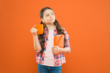 Breakfast the most important meal of the day. Little child having breakfast on orange background. Cute pupil holding book and drink for breakfast. Small girl thinking during her school breakfast